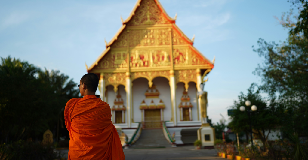 Buddhist monk walking beside a traditional temple in Laos