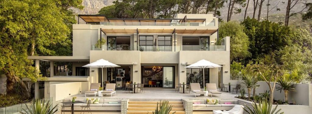 A three storey contemporary villa with terraces and a pool deck, framed by trees with a mountain cliff face rising behind it.