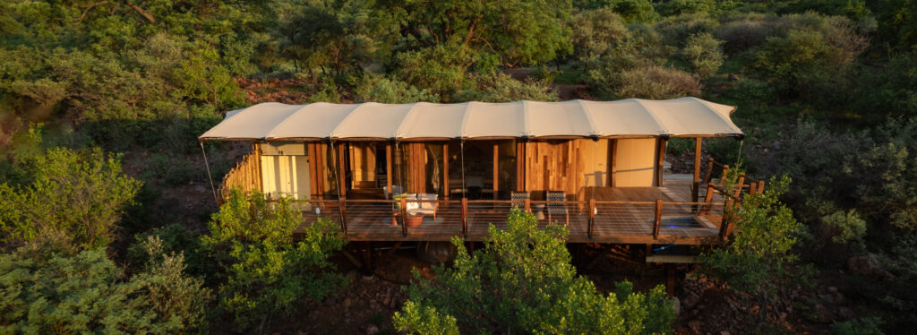 A tented suite on a raised wooden deck, set above a wooded gorge with rocky hills beyond.