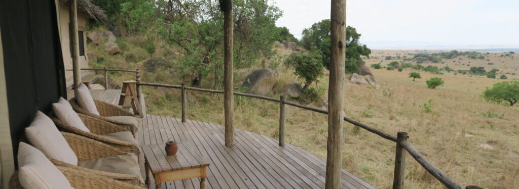 A thatched deck with wicker armchairs overlooking rocky outcrops and open savannah plains stretching to the horizon.