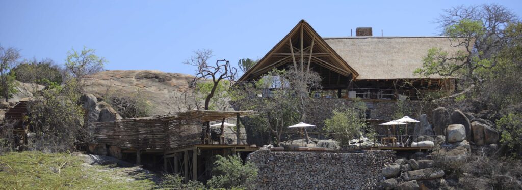 A thatched lodge with stone walls and umbrella shaded decks, built into a granite kopje among boulders and acacia trees.