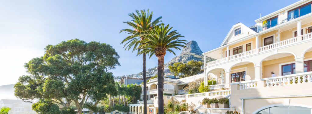 A landscaped garden with palm trees and a swimming pool below a cream colonial style hotel, with Lion's Head peak visible beyond.